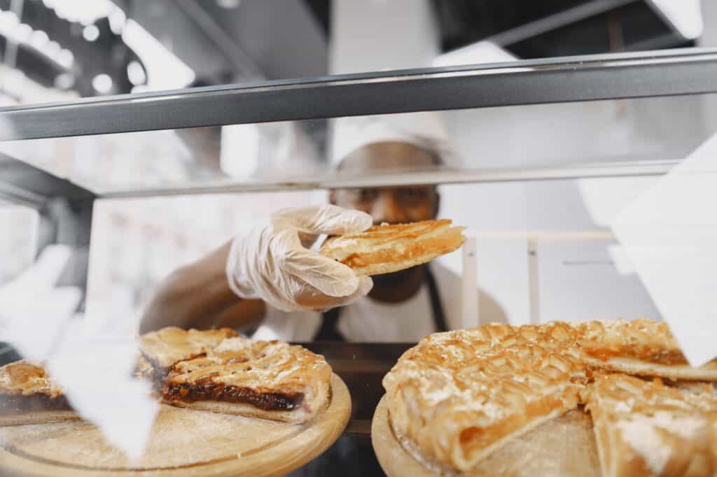 A baker arranging slices of pies for display in a bakery